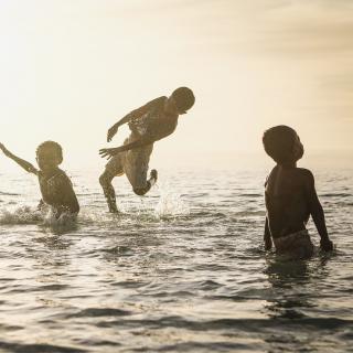 four small humans splashing and jumping in water