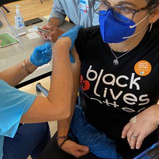 A UU woman in a Black Lives Matter T-shirt gets a COVID vaccine.