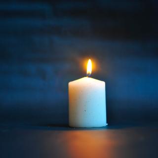 A white pillar candle is lit against a dark blue background.