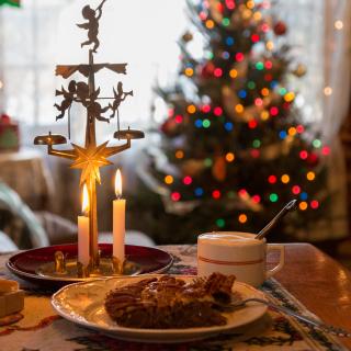 In the foreground, a slice of pecan pie and a hot beverage sit on a table. In the background, there's a merry decorated Christmas tree.