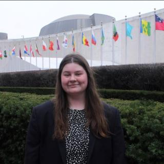 White woman with brown hair wearing a dark blazer in front of the line of national flags outside the United Nations Headquarters