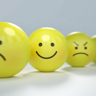 four yellow balls, one with a frown face, one with a smile face, one with a worried face, one with an angry face