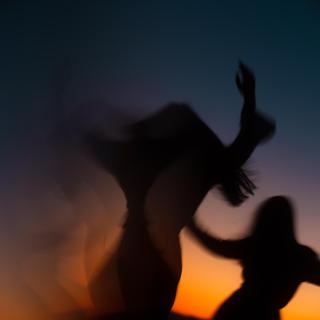 Against a sunset and dark sky, two figures appear to be dancing ecstatically. 