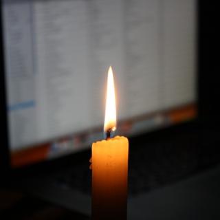 A single candle burning with a laptop in the background.