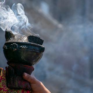 A hand holding a censer, in which burning copal incense releases smoke.