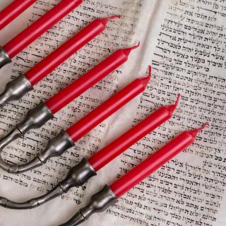 A menorah with red candles lies on the open pages of Hebrew scripture.