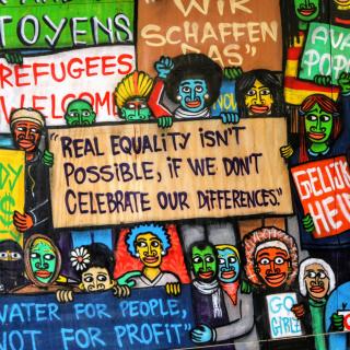 Street-art mural of multicolored smiling people holding signs, including "Real Equality Isn't Possible, If We Don't Celebrate Our Differences," "Refugees Welcome," "Nobody Eats Money," "Water for People, Not for Profit," and "Coexist"