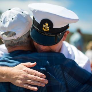 A hug between naval officer and an older man in a ball cap