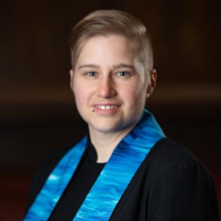 Rev. Lane-Mairead in their formal portrait, wearing a black clergy robe and blue stole.