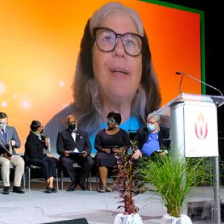 UUs seated on general session stage with image of Meg Riley projected on a scree in background