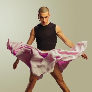 A gender fluid male, with very short hair, an earring, and makeup, with skirt fluttering in air