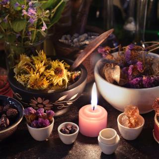 An altar with a lit candle, crowded by jars of herbs and flowers and other ritual objects