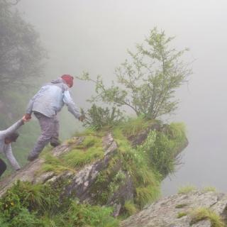 On a rocky outcrop in what appears to be inclement weather, one person strenuously pulls another person uphill.
