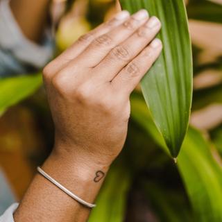 A broad, green leaf held by a Black woman's hands. A small tattoo of a heart is on her wrist.