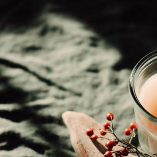 A lit candle in moody lighting with a sprig of red berries