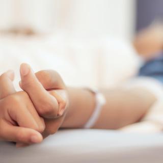 A close-up of a hand holding the hand of a patient lying in a hospital bed.