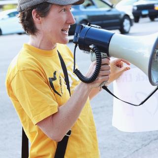 person in a hat holding a bullhorn and wearing a yellow Side With Love shirt