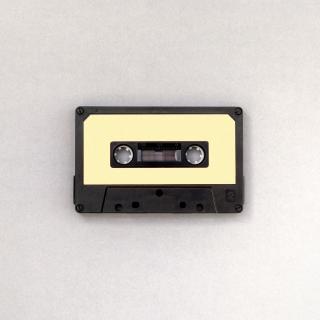 A single cassette tape, black with a blank yellow label, on a white surface.