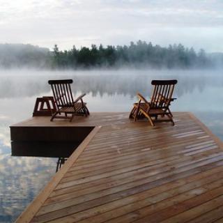 A lake covered by morning mist with two empty deck chairs at the end of a dock.