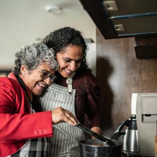 A Latinx mother and daughter embracing while cooking in the kitchen at home