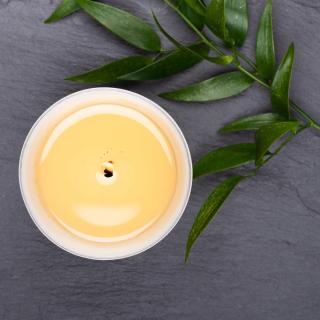 Seen from above, an ivory pillar candle burns on a slate surface with a branch of greenery resting nearby.