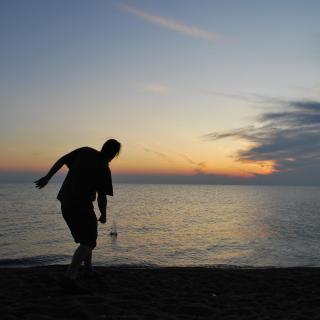Silhouetted by the setting sun, a person is caught in the moments after skipping a stone into Lake Erie at Point Pelee National Park, Ontario.