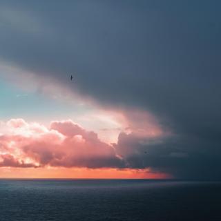 A dark cloud gives way to blue sky and vivid sunet over a gray ocean