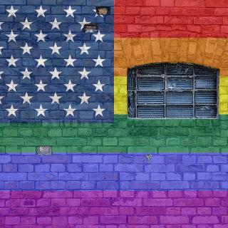 Image of a brick wall painted like an american flag, with the stripes the colors of the rainbow.