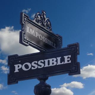 intersecting street signs, with the words "impossible" and "possible," in front of blue sky and clouds background