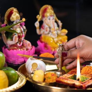 a person touches a Ghanti bell on a Hindu altar, in front of statues of Ganesha and Lakshmi 