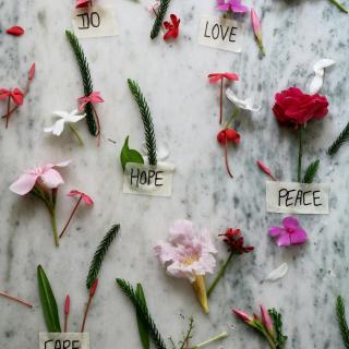 An arrangement of various flowers and leaves on a marble top with the words "DO", "LOVE", "HOPE, "PEACE", "CARE", and "LIVE" written in black sharpie on pieces of masking tape.