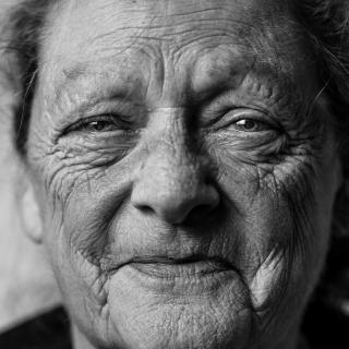 Black and white photo of the face of an older white woman, who looks like she is suppressing a smile.