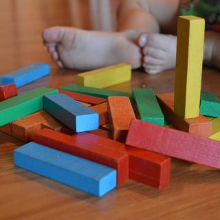 set of colorful wooden blocks on a wooden floor with a set of toddler feet beside them.