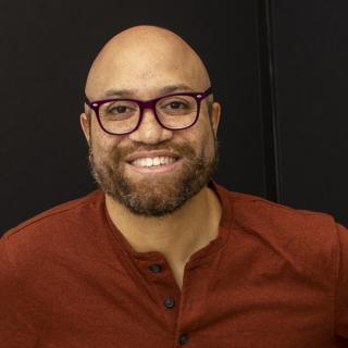 Darrick Jackson is smiling, wearing a red shirt and glasses