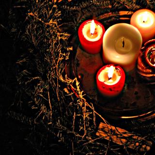 From above, an arc of a thick evergreen wreath. In its center, four red pillar candels are lit; the white pillar candle at the center is unlit.