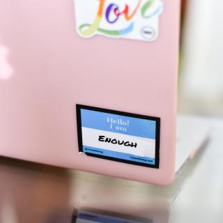 On the back of a pink MacBook, a nametag that says "Hello! I am..." and written in below: "Enough."
