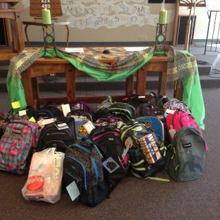 In front of a church altar, about a dozen school backpacks are stacked up.