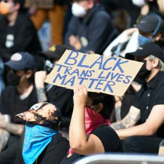 In a sea of protestors wearing black, a person holds a sign reading "Black trans lives matter."