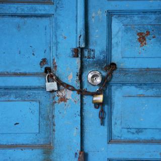 Two vivld blue wooden doors are locked with a heavy chain and two padlocks
