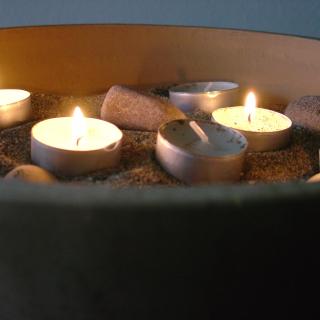 Several tea lights burn in a bowl of sand