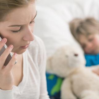 A woman speaks on a cell phone while, in the background, a child sleeps with a teddy bear