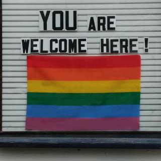 An outdoor sign that says "YOU are welcome here!" with a rainbow flag.