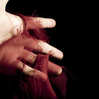 A human hand holds a fraying, spooled piece of red silk