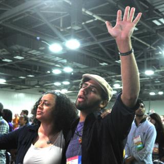 Two worship attendees stand arm in arm, with other hands raised.
