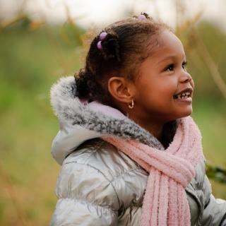 A young girl, bundled into a warm coat, smiles excitedly at someone off-camera.