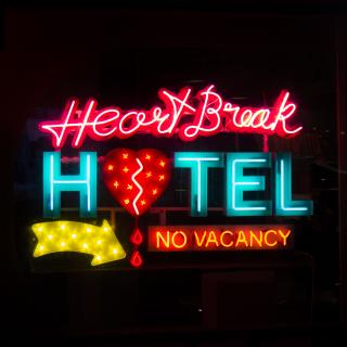 A colorful neon sign, "Hearbreak Hotel" (the "o" in hotel is a broken heart) with a yellow arrow and "no vacancy"
