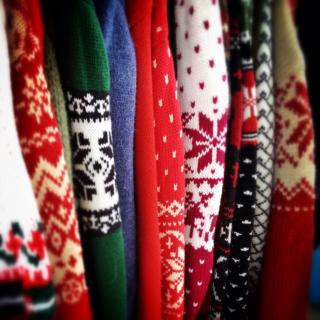An assortment of brightly colored holiday sweaters, in profile, lined up as they hang together