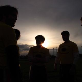 Against a setting sun, five people form a circle, visible only as silhouettes
