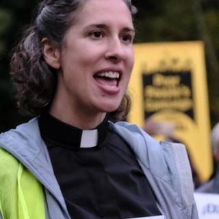 Rev. Jodi speaks, wearing a clergy collar, with a Poor People's Campaign banner behind her.