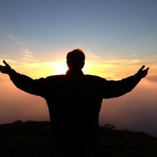 A person reaches their arms to the sky as the sun rises.